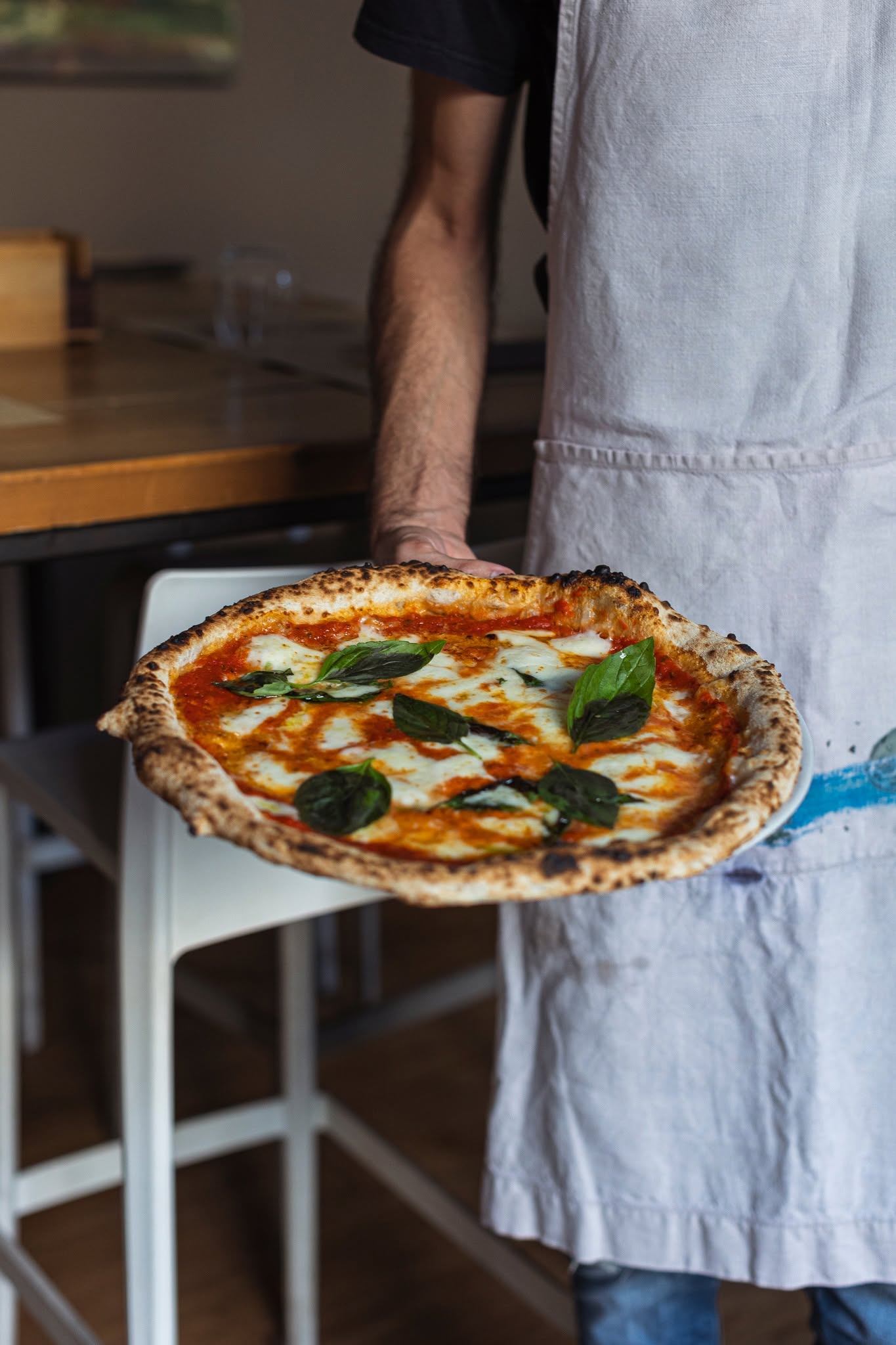Un pizzaiolo di Frumento porge una margherita appena uscita dal forno